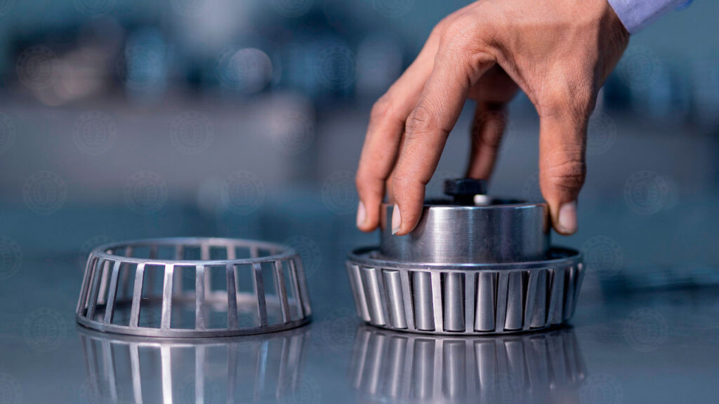 Close-up of a technician's hand carefully assembling a precision tapered roller bearing with its metal cage. Proper component selection and precise cage alignment during manufacturing help prevent premature bearing failure.